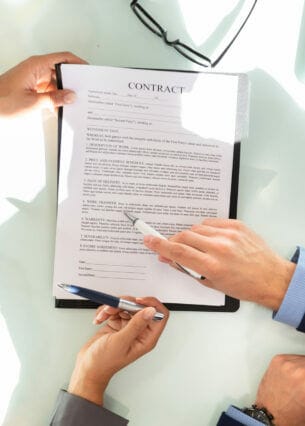 Ein Vertrag auf einem Tisch, dem sich zwei Personen mit je einem Kugelschreiber in der Hand zuwenden