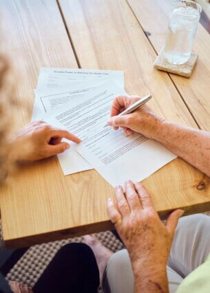 Zwei Personen an einem Tisch, von denen eine Dokumente unterzeichnet
