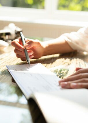 Eine Person sitzt an einem Tisch und unterschreibt einen Scheck