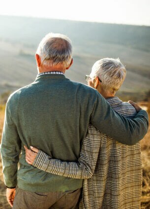 Zwei ältere, sich umarmende Menschen, die zwei Erwachsenen mit zwei Kindern hinterherblicken