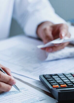 Nahaufnahme von den Händen einer Person, die mit der einen Hand ein Formular ausfüllt und in der anderen Hand einen kleinen Zettel hält.