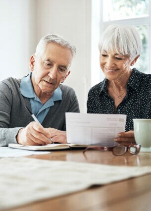 Zwei ältere Personen sitzen an einem Tisch und gehen Dokumente durch