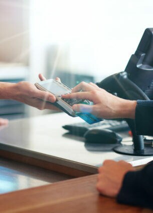 Eine Person, die über einen Tresen, auf dem ein Kaffeebecher steht, Zahlen in ein Terminal eingibt, das eine Person auf der anderen Seite des Tresens hinhält