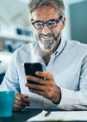 Eine Person sitzt an einem Tisch und hält dabei ein Smartphone in der Hand, aus dem Raster kommen, die sich über ihr Gesicht legen