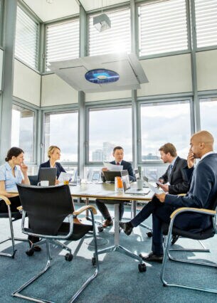 Fünf Personen, drei Männer und zwei Frauen, sitzen rund um einen Tisch in einem hellen Konferenzraum