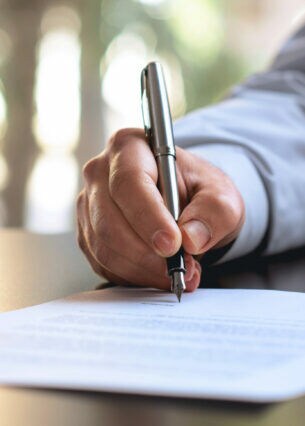 Detailaufnahme einer Hand, die einen Stift hält und ein Dokument unterzeichnet