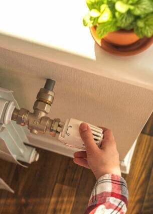 Eine Person dreht am Thermostat eines Heizkörpers