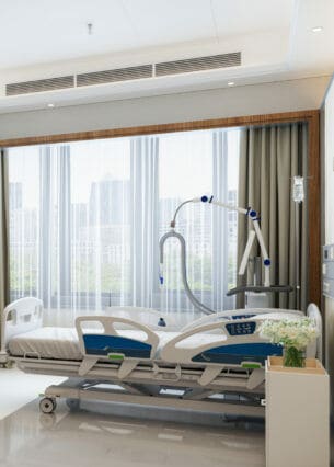 Modernes Luxus-Krankenhauszimmer mit leerem Bett, LCD-Fernseher und Stadtblick aus dem Fenster