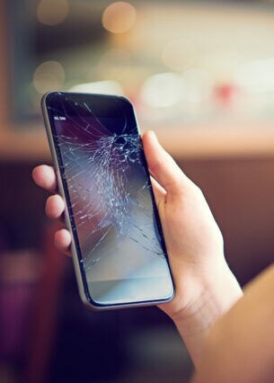 Eine Person betrachtet das Display ihres Smartphones, das zersprungen ist.