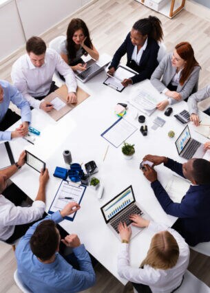 Eine Gruppe von zwölf Personen sitzt mit Laptops an einem Tisch.