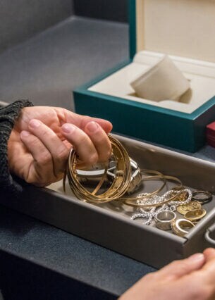 Nahaufnahme einer Person, die goldene Schmuckstücke aus einem Bankschließfach entnimmt