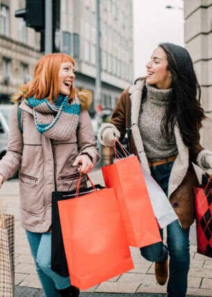 Zwei Personen gehen lachend mit Einkaufstüten über eine Straße.