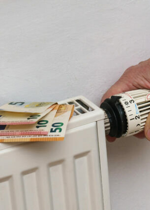Eine Person dreht an einer Heizung, auf der Geldscheine liegen.