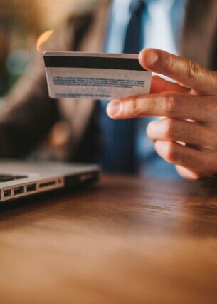 Nahaufnahme einer Hand, die neben einem geöffneten Laptop eine Kreditkarte in der Hand hält.