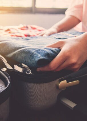 Eine Person legt eine Jeans in einen aufgeklappten Koffer.