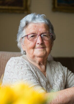 Porträt einer älteren Person, die auf ihrem Sessel sitzt und in die Kamera blickt.