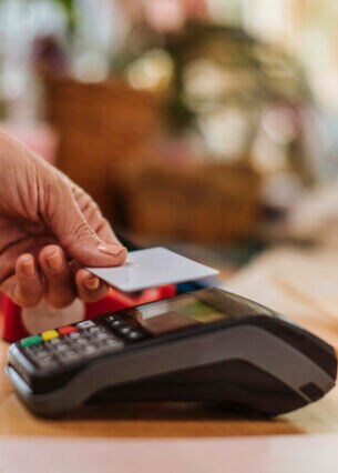 Eine Person hält eine Karte zum Bezahlen an ein Kartenlesegerät.