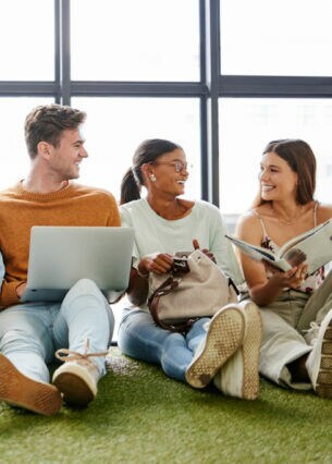 Mehrere junge Personen sitzen nebeneinander auf dem Fußboden an eine Fensterfront gelehnt.