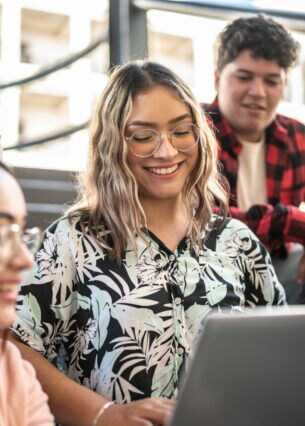 Mehrere junge Personen sitzen in einem Hörsaal um ein Laptop herum.