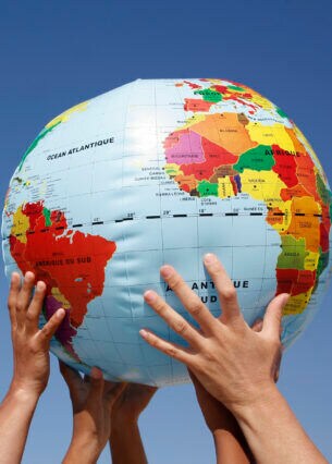 Mehrere Hände halten einen Ball mit Weltkugelmotiv in die Höhe.