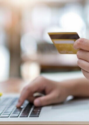 Nahaufnahme einer Hand, die eine Bankkarte hält, die andere Hand liegt auf einer Laptoptastatur.