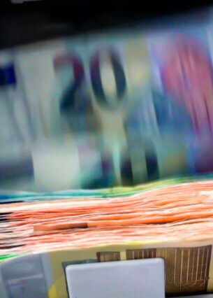 Ein Bündel Geldscheine wird von einem Geldautomaten ausgegeben. Unten liegt ein Stapel 200-Euro-Scheine, der Automat gibt noch 20-Euro-Scheine aus