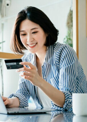 Eine Frau sitzt vor dem Laptop und schaut auf eine Kreditkarte