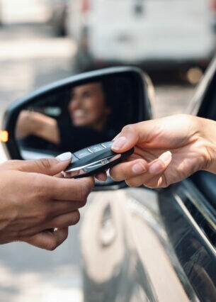Eine Person sitzt im Auto und bekommt durchs geöffnete Fenster einen Autoschlüssel gereicht.