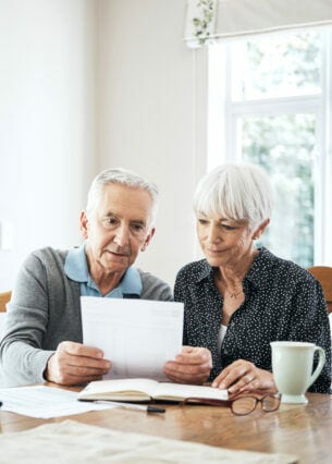 Zwei ältere Personen sitzen am Tisch und schauen gemeinsam auf Rechnungen.