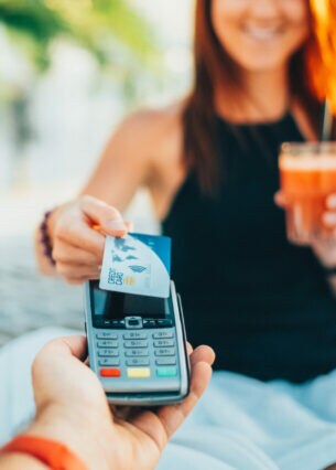 Eine Person in einer Hängematte hält ein Getränk in der Hand und bezahlt mit einer Kreditkarte.