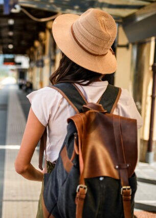 Eine Person in Rückansicht mit Rucksack und Hut steht am Bahnsteig.