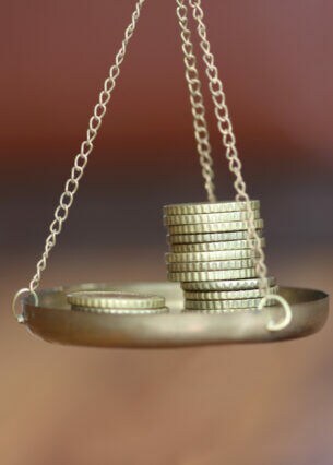 Nahaufnahme einer Waagschale, auf der zwei Münztapel liegen.