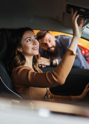 Eine Person sitzt im Auto und betätigt vor dem Rückspiegel ein paar Knöpfe.