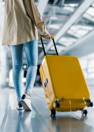 Eine Person in der Rückansicht zieht im Flughafen einen Koffer hinter sich her.