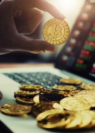 Ein Laptop mit Aktienkursen und einer Hand, die eine Bitcoin-Münze hält.