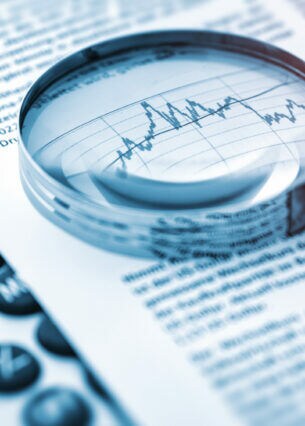 Eine Lupe liegt auf einem Blatt Papier mit Aktienkursen.