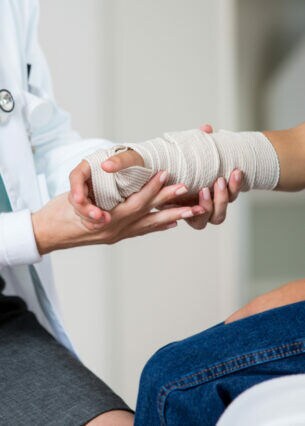 Nahaufnahme eines Arztes, der einen einbandagierten Arm untersucht.