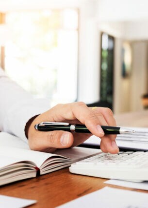 Nahaufnahme einer Hand, die einen Stift in der Hand hält und parallel auf einem Taschenrechner tippt.