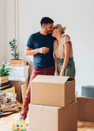 Zwei Personen stehen zwischen Umzugskartons und umarmen sich.