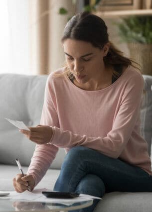Eine Person sitzt auf einem Sofa und trägt etwas auf einem Blatt Papier ein.
