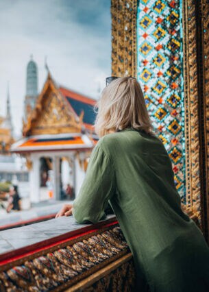 Eine Person blickt aus einem prunkvoll verzierten Fensterrahmen auf goldbesetzte Tempel.