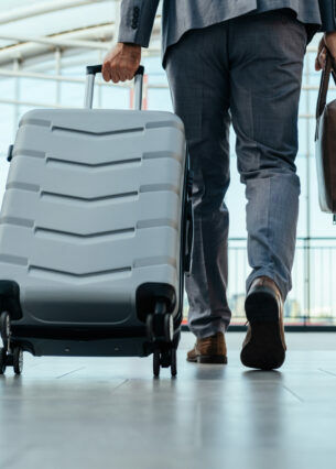 Ein Mann im Anzug geht mit einem Rollkoffer und einer Laptoptasche durch eine Halle.