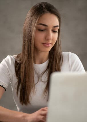 Eine junge Frau sitzt vor einem aufgeklappten Laptop.