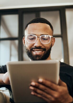 Ein Mann sitzt auf einem Sofa und hält ein Tablet in der Hand.
