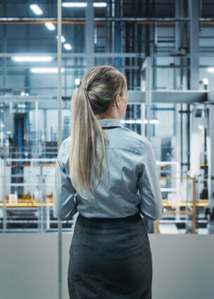 Eine Person blickt durch eine Glaswand auf eine durch Roboter gesteuerte Fertigungskette.