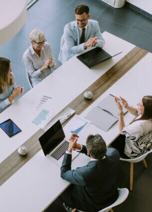 Mehrere Personen sitzen mit Laptops und Papieren und Mappe an einem Tisch.