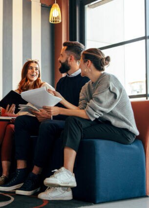 Mehrere Personen sitzen in einem loftartigen Büro zusammen auf einer Couch.
