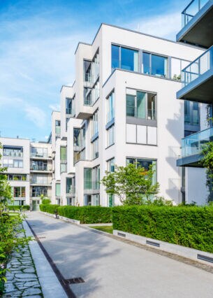 Neubauten mit quaderförmigen Häusern, asphaltiertem Gehweg und Hecken.