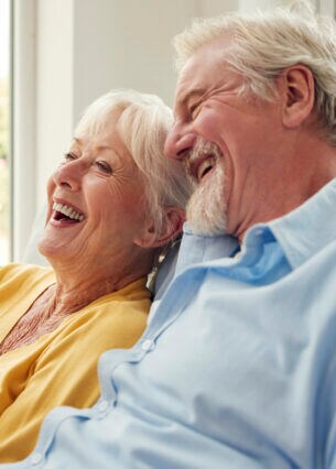 Ein Paar sitzt eng aneinandergekuschelt auf einem Sofa, eine von ihnen hält eine Tasse in den Händen.