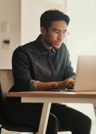 Eine Person sitzt vor einem geöffneten Laptop am Tisch.
